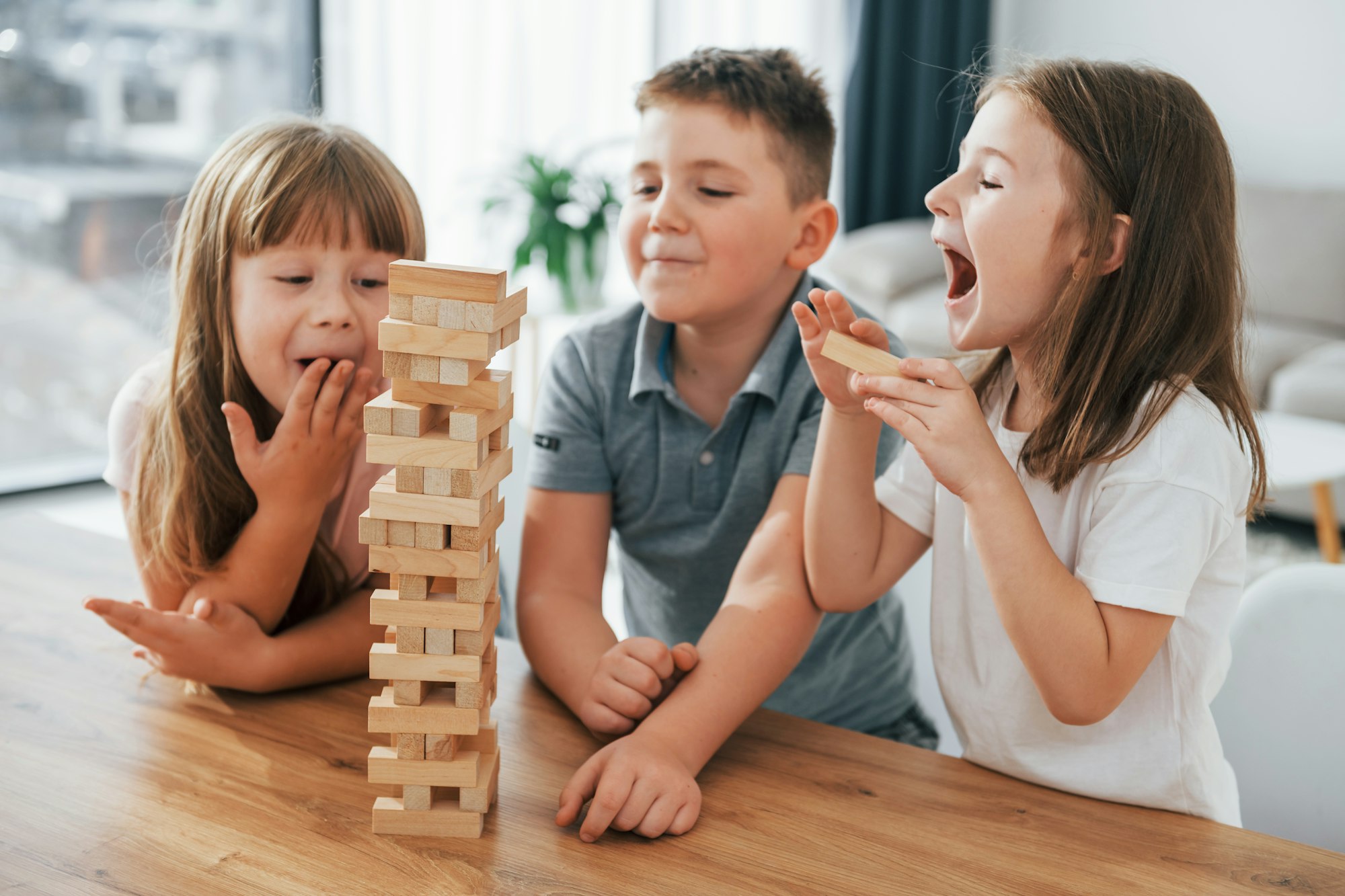 Focused on the jumbling tower game. Kids having fun in the domestic room at daytime together